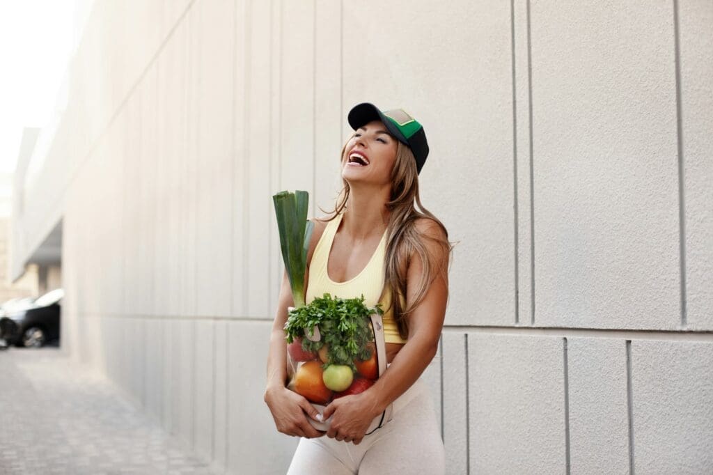 A sporty girl smiles and holds a bag full of fresh fruits and vegetables. Healthy lifestyle, health,