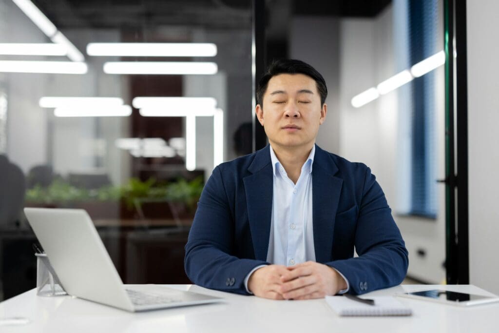 Professional businessman meditating at office desk to reduce work stress