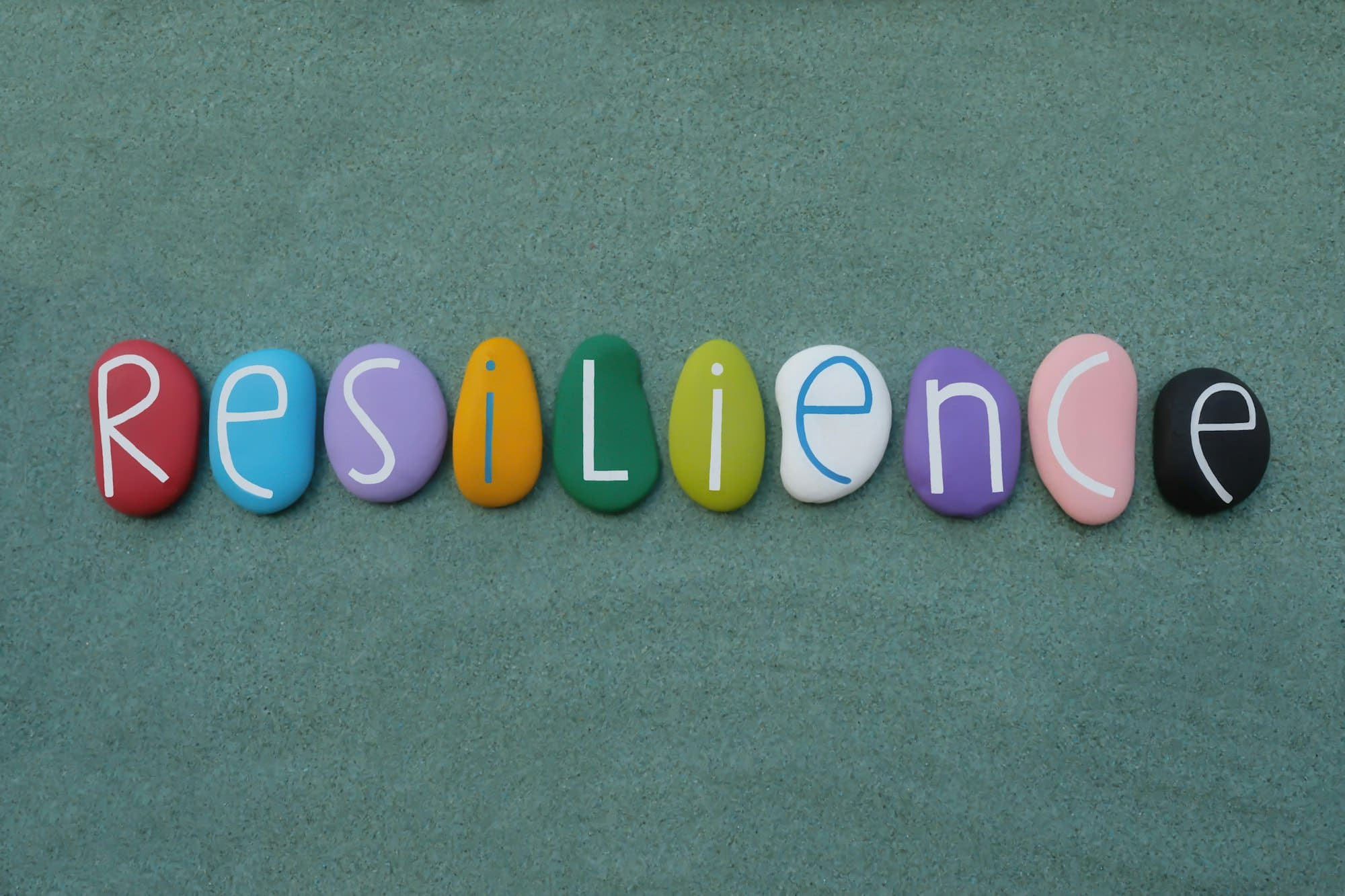 Resilience word composed with multicolored handmade painted stone letters over green sand