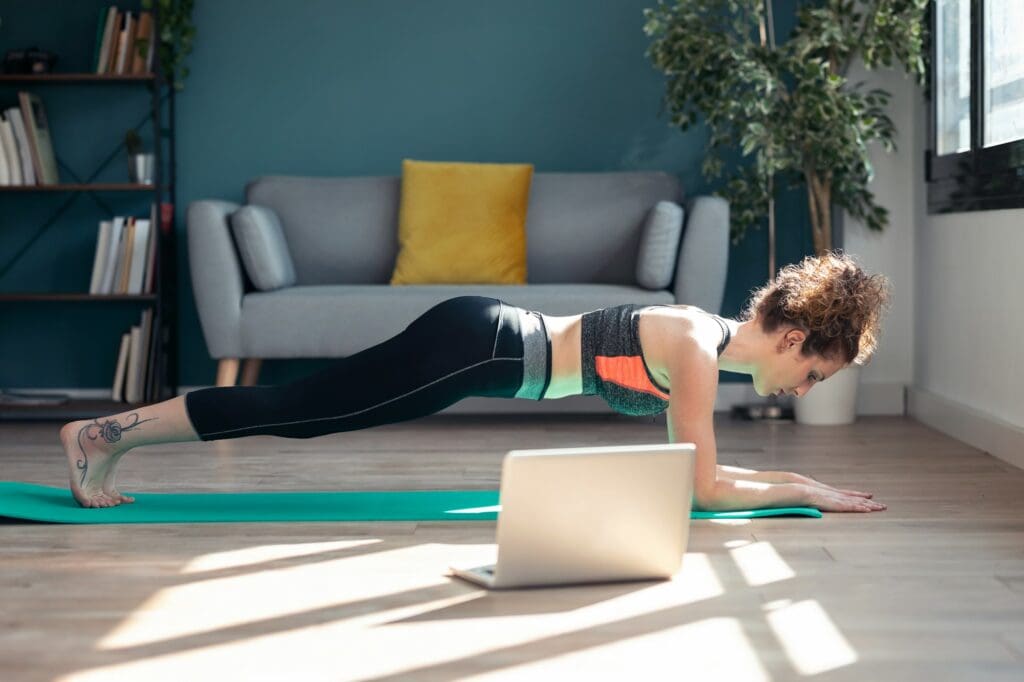 young woman doing exercises following online gym classes via laptop at home.